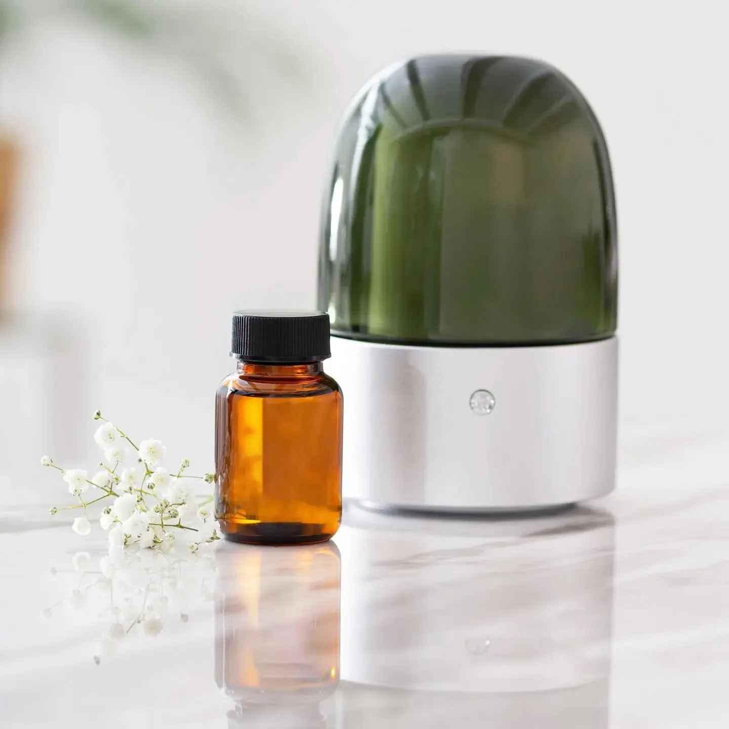 Green diffuser and amber bottle with flowers on a light surface