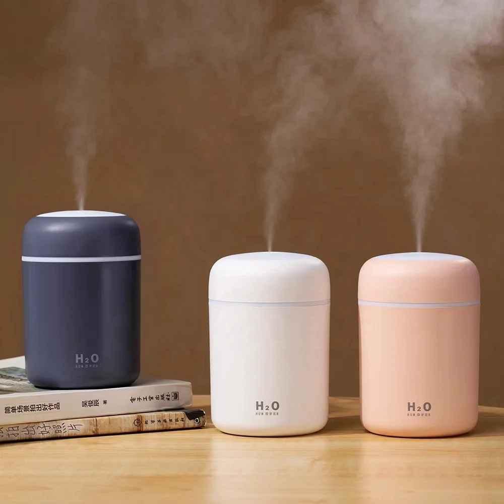 Three H2O humidifiers in black, white, and pink on a wooden table with steam rising.