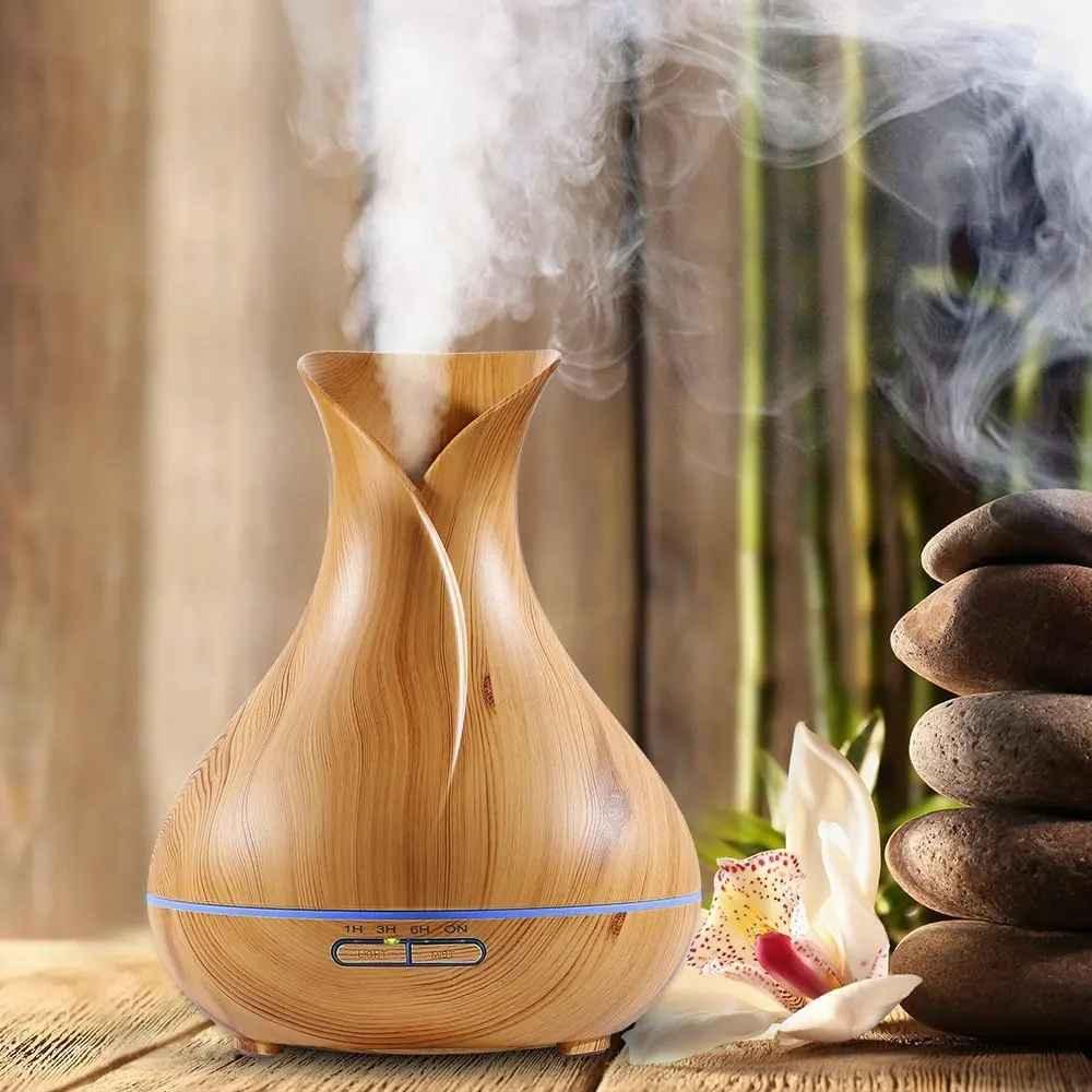 Wooden diffuser emitting steam on a wooden surface with stones and flowers in the background