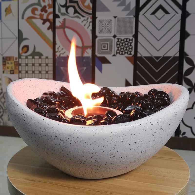 Modern tabletop concrete fire bowl with black stones and flame, decorative patterned wall