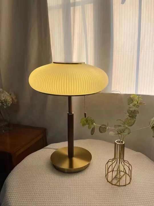Modern gold table lamp with ribbed glass shade on round table near decorative vase