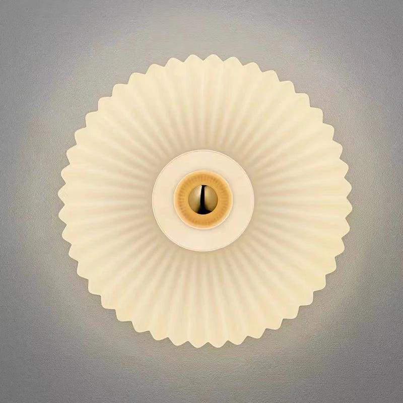 Round pleated wall lamp with warm light on gray background, modern lighting decor
