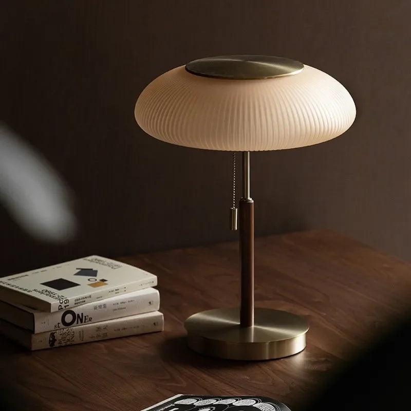 Modern brass table lamp with ribbed glass shade on wooden desk beside stacked books