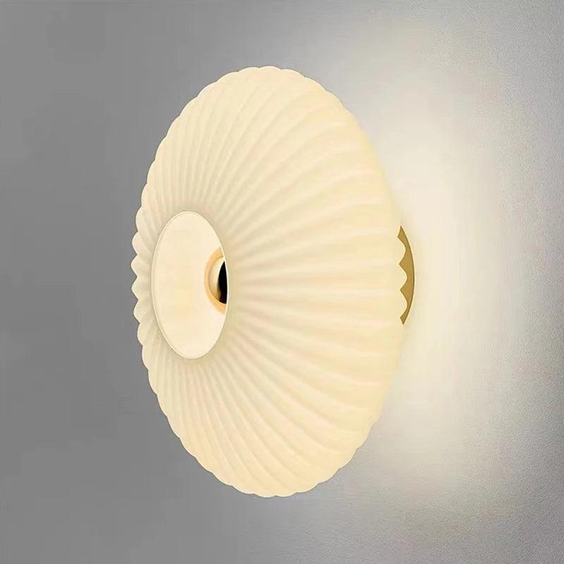 Modern pleated round wall sconce with warm white light on a gray wall