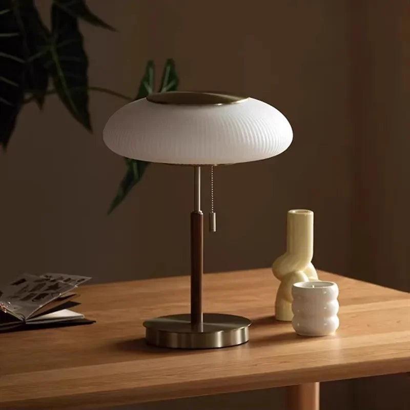 Modern table lamp with white glass shade on a wooden desk, decorative vase and cup nearby