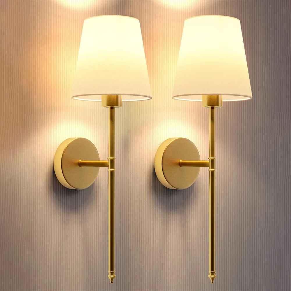 Pair of modern gold wall sconces with white lampshades on textured wall