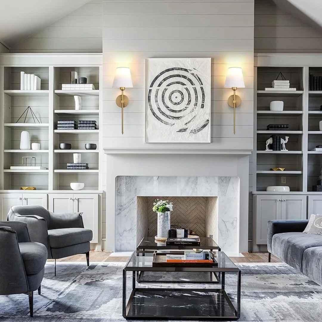 Modern living room with grey armchairs, marble fireplace, built-in bookshelves, and abstract wall art