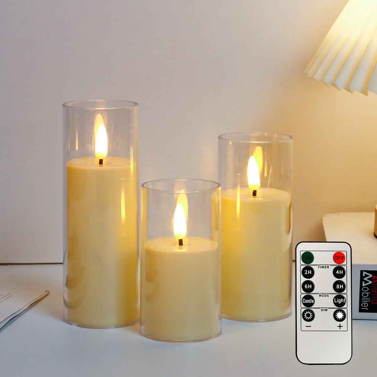 Set of three flameless candles with a remote control on a table.