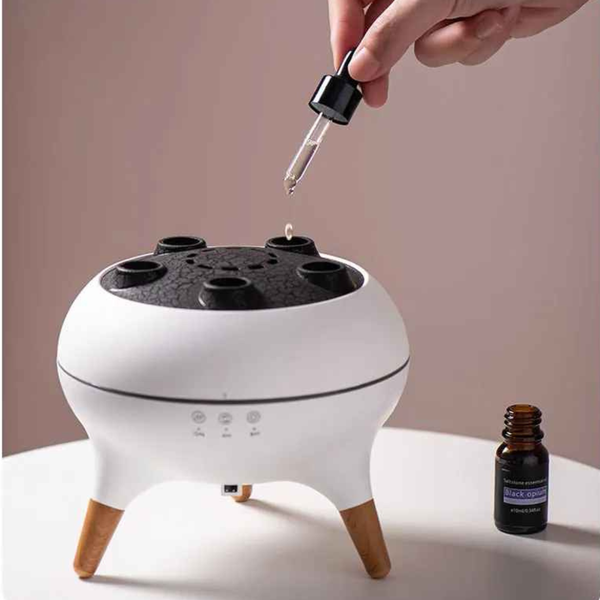 White essential oil diffuser with a hand using a dropper and a bottle of essential oil on a light background