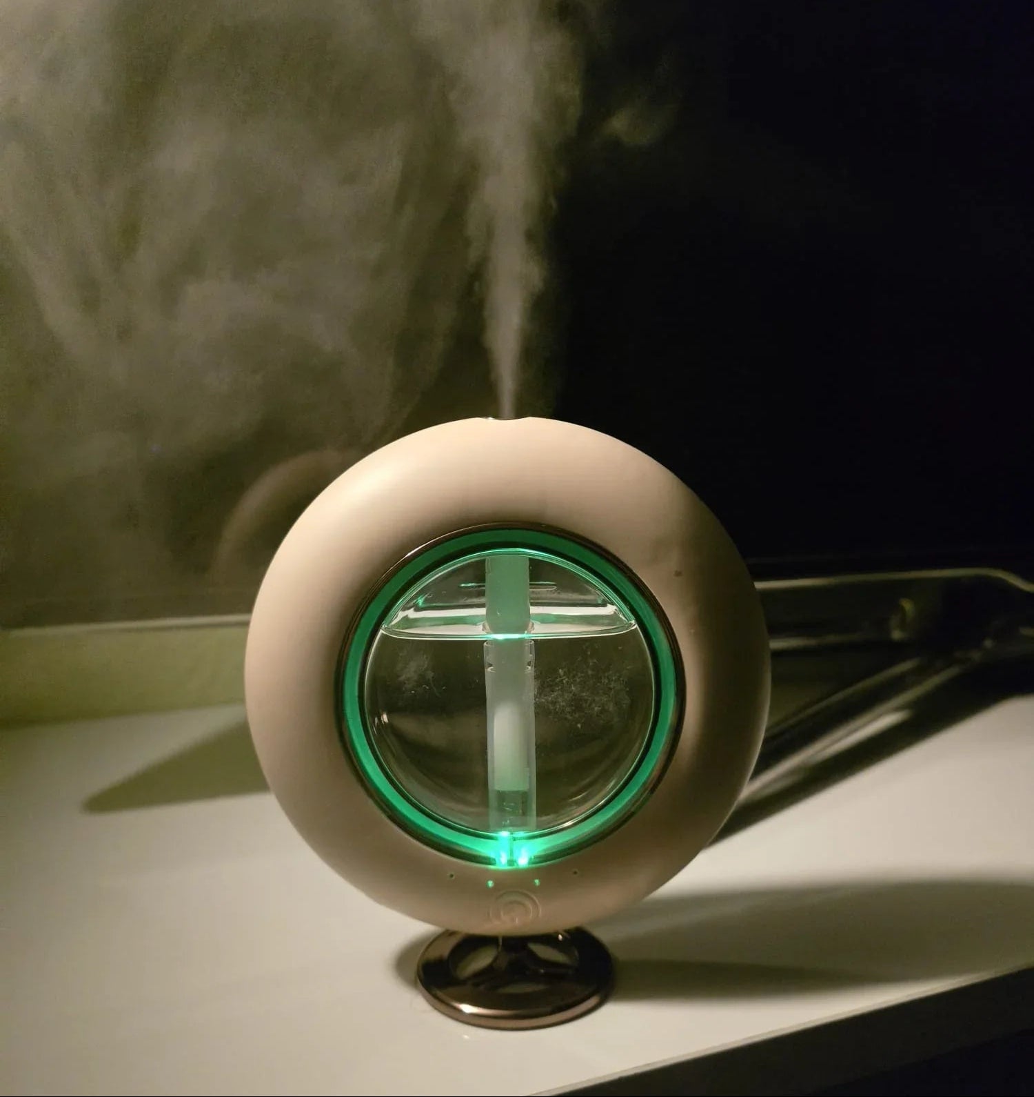 Modern round humidifier with green light emitting vapor on a white table