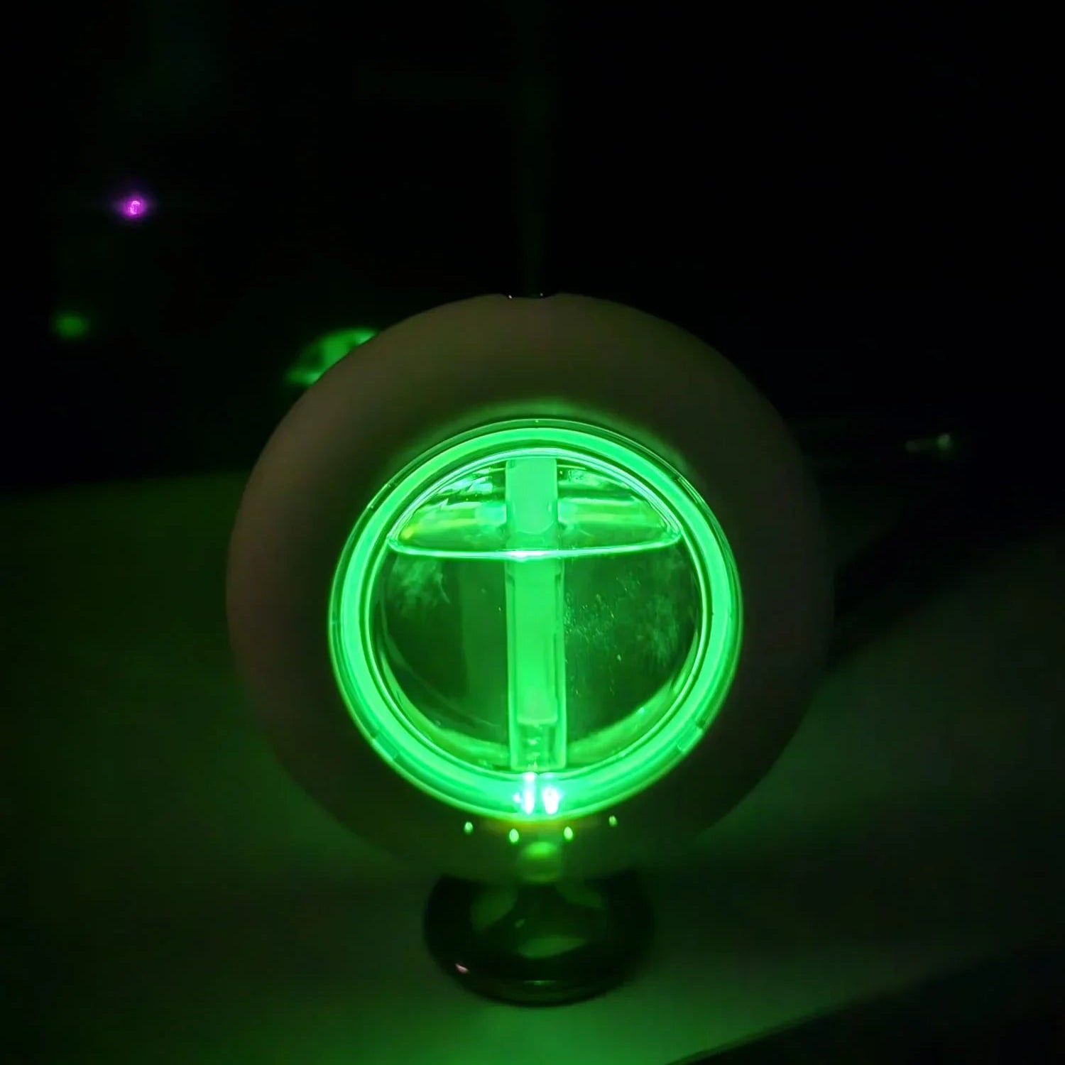 Modern round humidifier with green LED light in dark room, mist rising from top