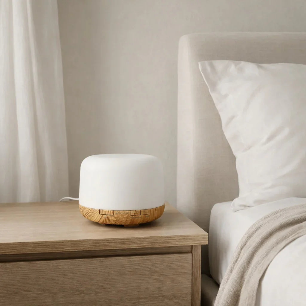 White diffuser on a wooden nightstand next to a bed with white bedding.